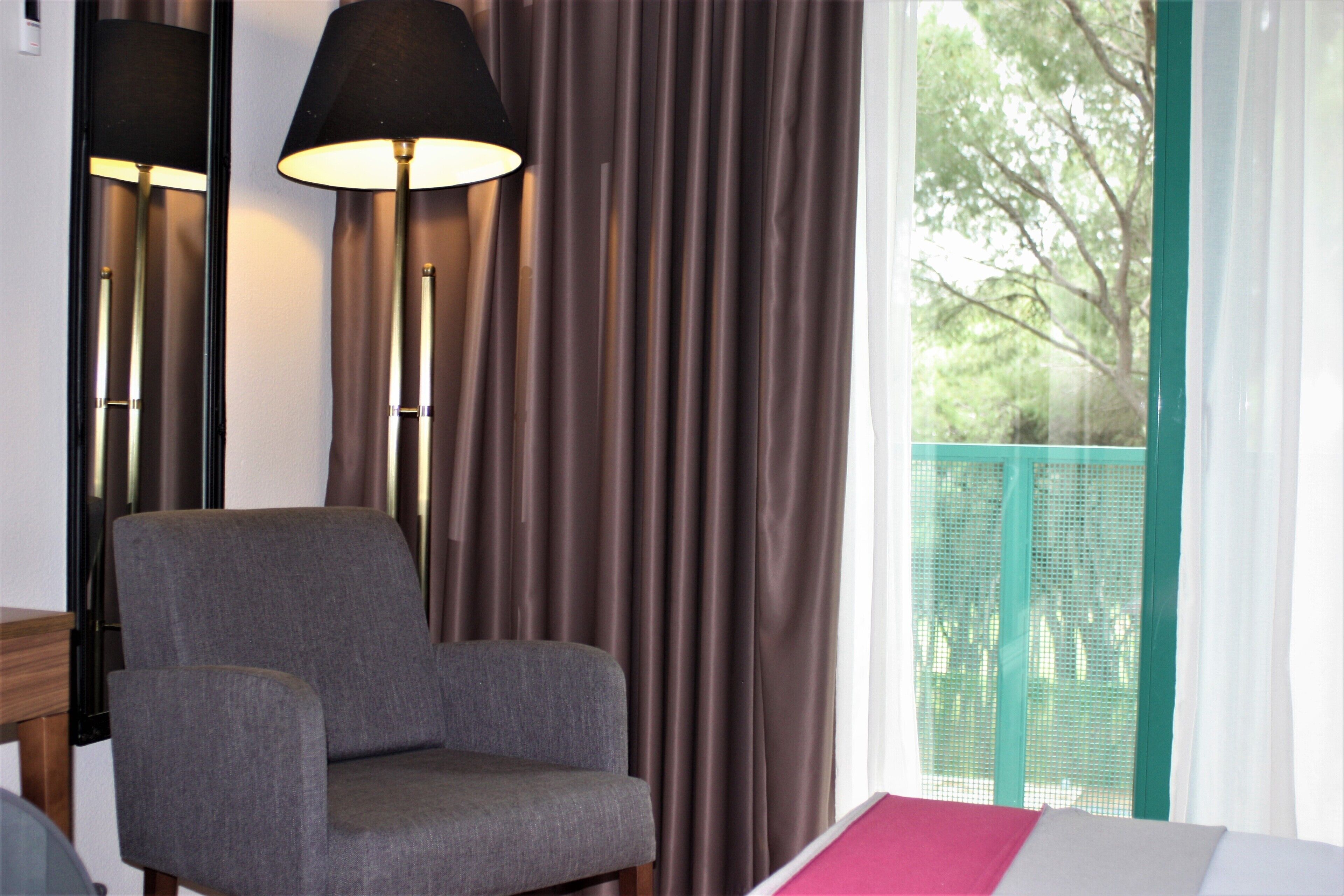 A room with a grey armchair, a floor lamp, and a window with curtains.