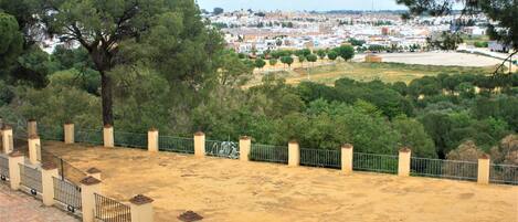 A view of a cityscape with a sandy area in the foreground, surrounded by trees and a metal fence.