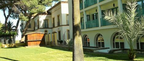 A multi-story building with a courtyard, featuring a large tree and a palm plant.