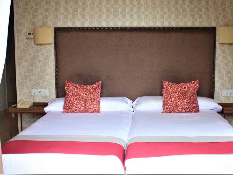 A double bed with a brown headboard, two bedside tables with lamps, and patterned pillows.