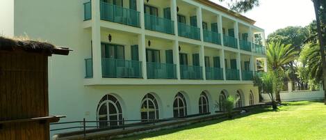 A multi-story building with balconies, a grassy courtyard, and a wooden structure to the left.