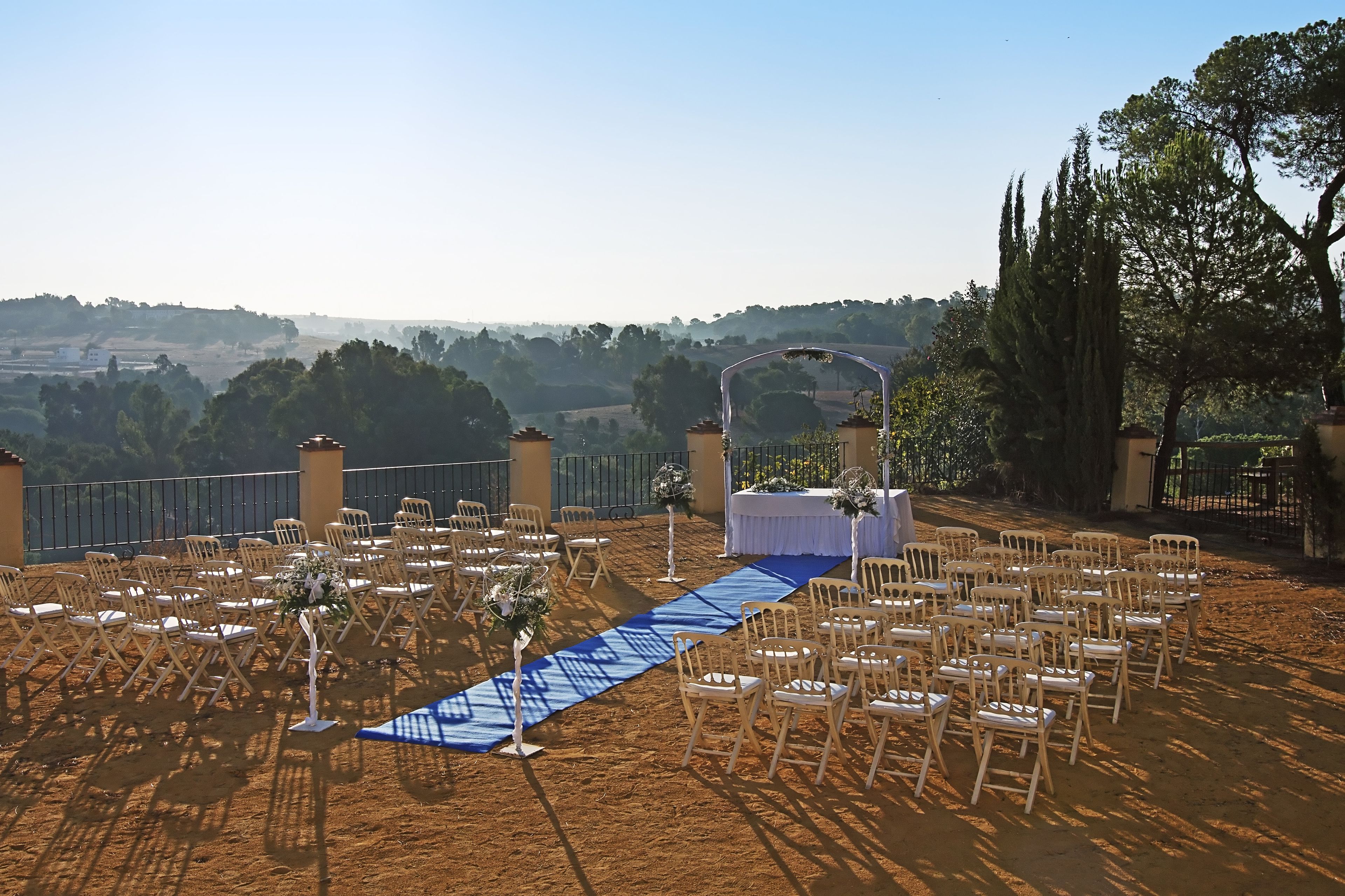 An outdoor wedding setup with rows of chairs and a blue aisle.
