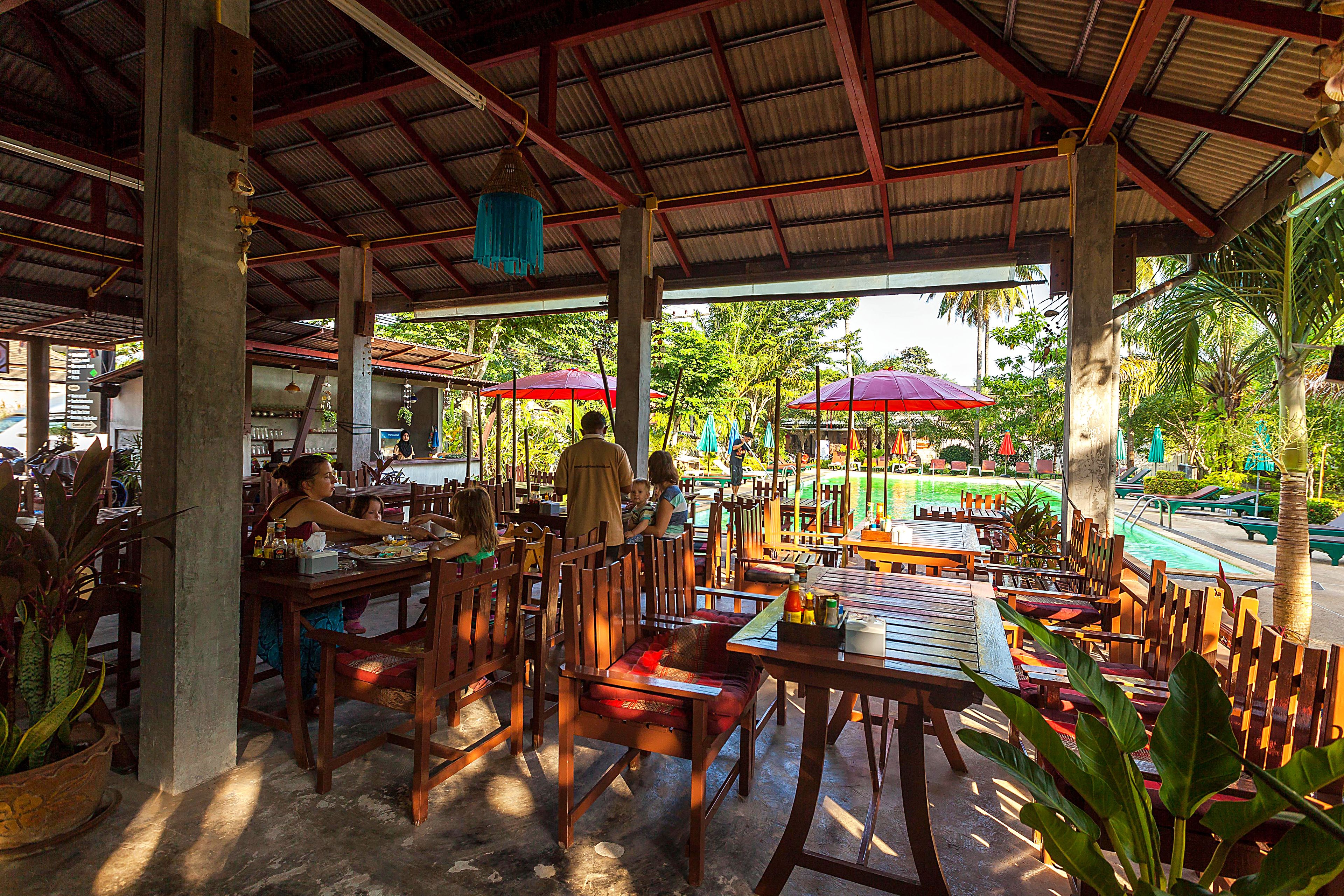 An outdoor restaurant with wooden tables and chairs, umbrellas, and potted plants.