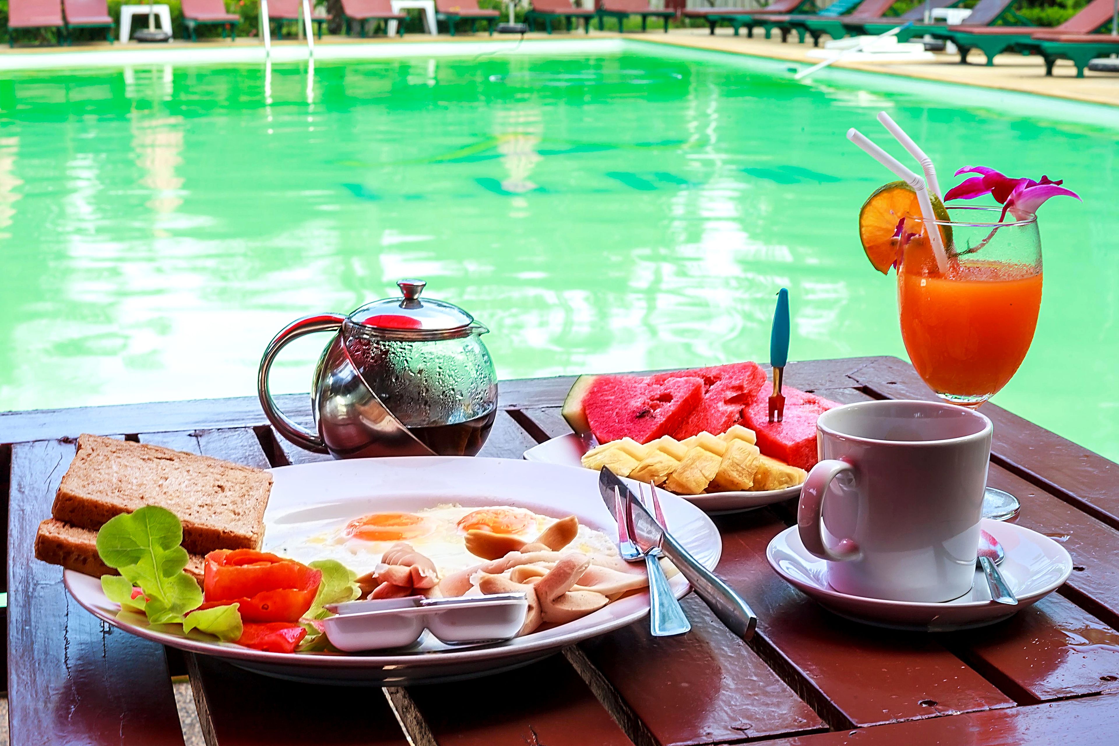 A breakfast setup with toast, eggs, fruit, and a drink by a pool.