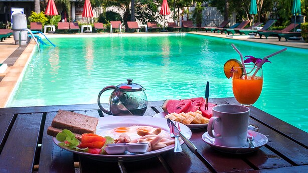 Desayuno junto a la piscina con una mesa, una tetera, un plato de comida, un vaso de zumo de naranja y una taza.