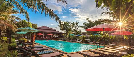 A pool area with lounge chairs and umbrellas, surrounded by greenery.