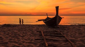 Un bote en una playa arenosa, con dos personas al fondo.
