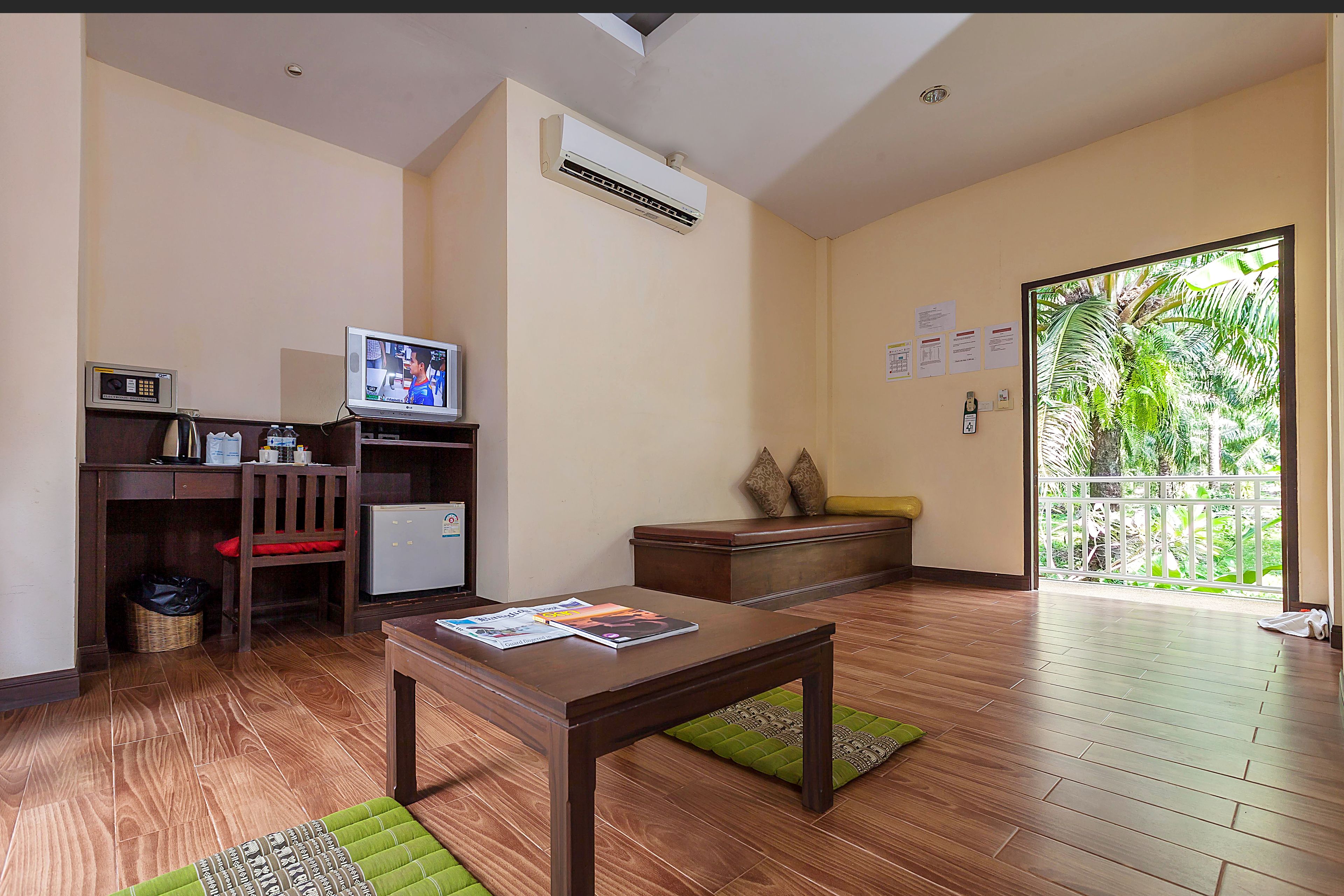 Una habitación con suelo de madera, un escritorio con computadora, un televisor y una ventana con vistas a zonas verdes.