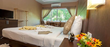 Une chambre d’hôtel avec un lit, une télévision, un bureau, une fenêtre avec des rideaux et un vase de fleurs.