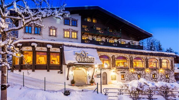 Un hotel con fachada cubierta de nieve, un balcón con luces y un letrero que dice "Hotel St. Georg".