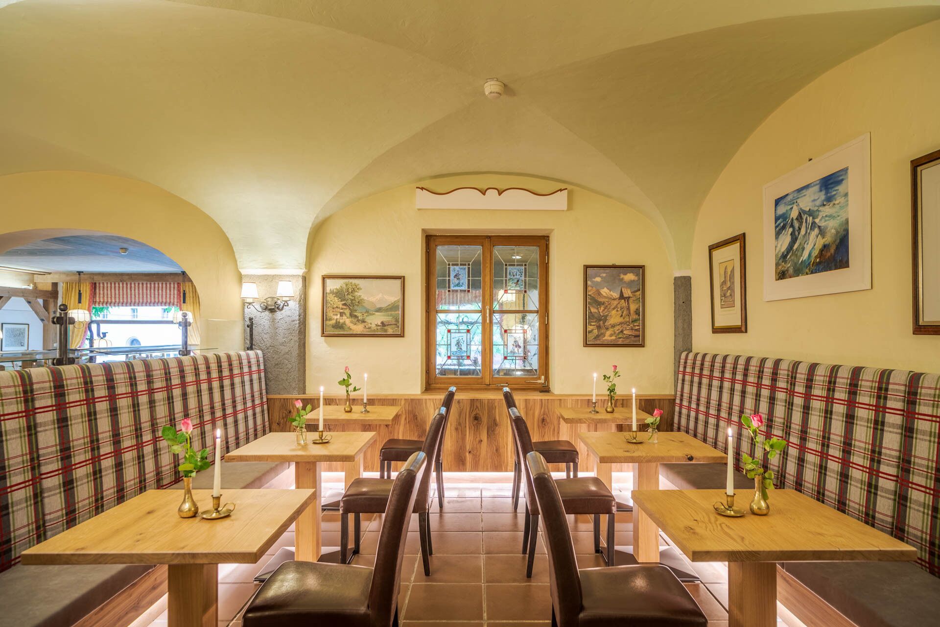 A restaurant with wooden tables and benches, arched ceilings, and framed artwork on the walls.