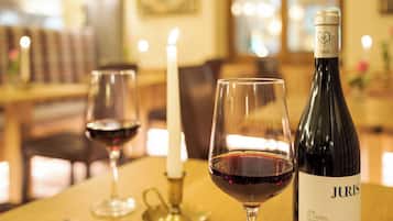 Una botella de vino Juris, dos copas de vino y una vela sobre una mesa de madera en una habitación con luz cálida.