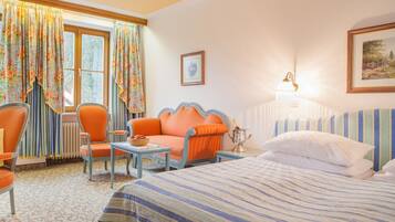 A hotel room with a bed, a chair, a table, and a window with curtains.