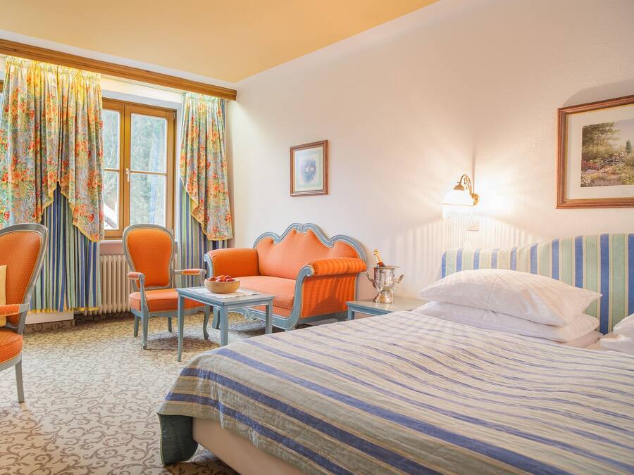 A hotel room with a bed, a chair, a table, and a window with curtains.