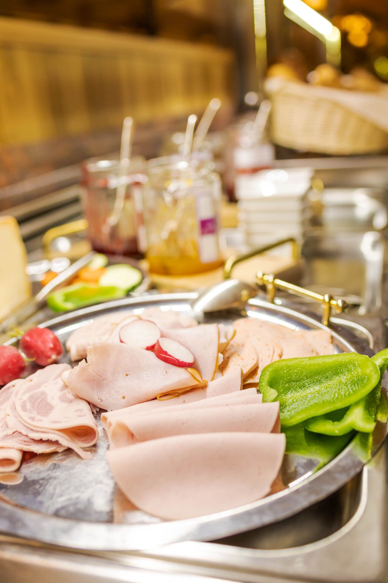 A buffet with sliced meats and vegetables on a metal tray.