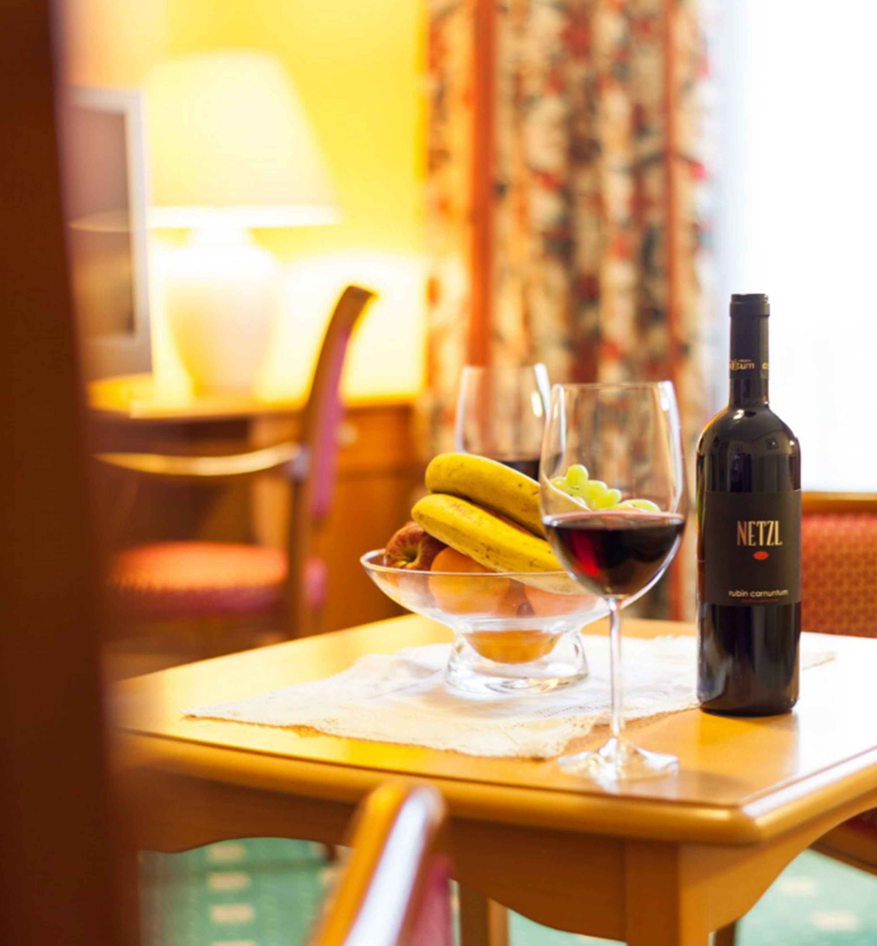 Ein Hotelzimmer mit Essbereich, gedeckt für eine Mahlzeit, mit einer Weinflasche, einem Weinglas und einer Obstschale.