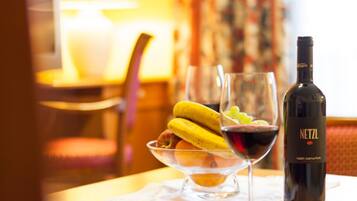 Ein Hotelzimmer mit Essbereich, gedeckt für eine Mahlzeit, mit einer Weinflasche, einem Weinglas und einer Obstschale.