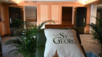 Un vestíbulo de hotel con un sofá verde, un cojín con el texto "Hotel St. Georg" y paneles de madera.
