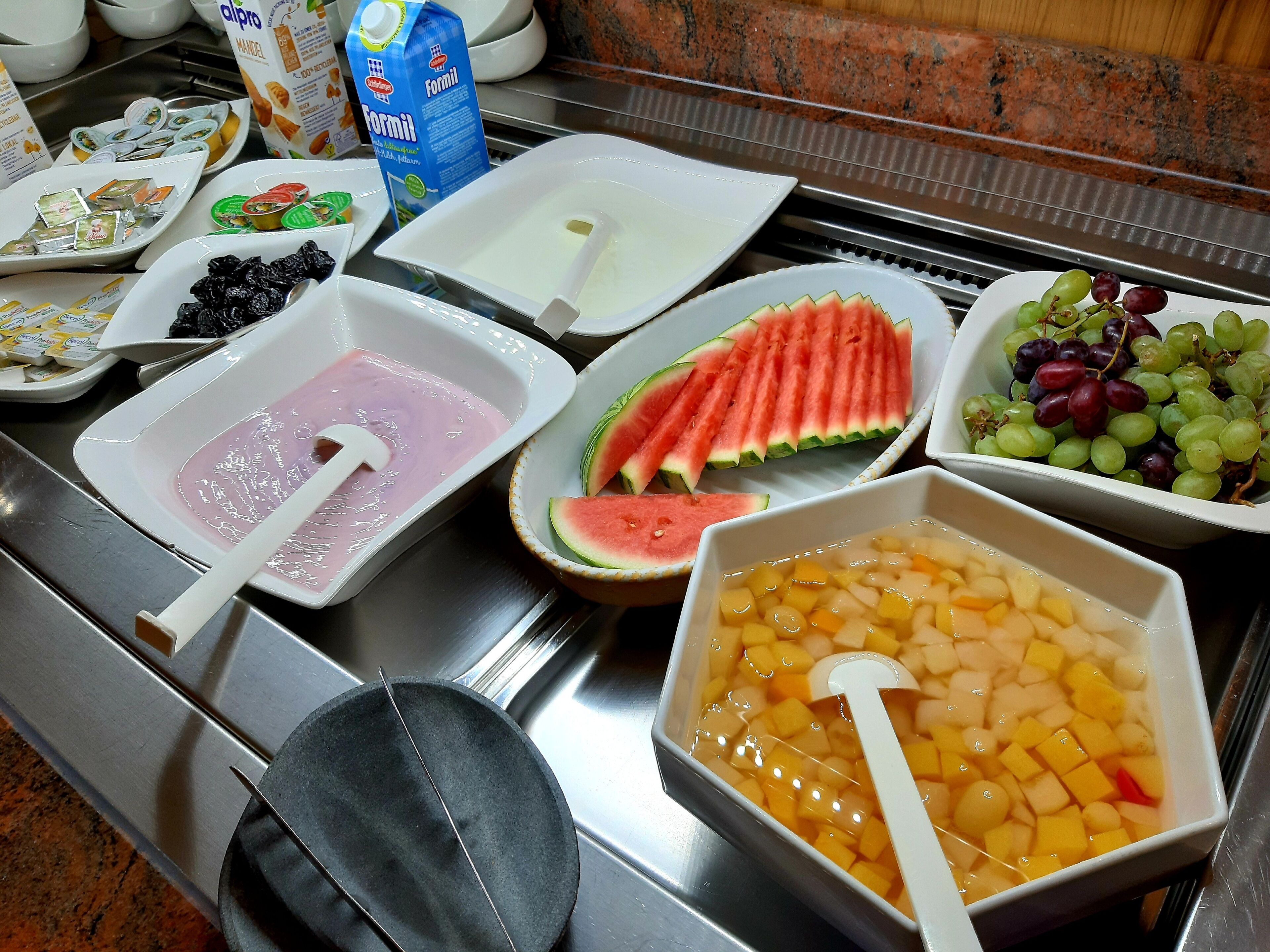 Un bufé con diversas opciones de comida, incluyendo rebanadas de sandía, uvas y ponche de frutas.