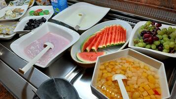 Un bufé con diversas opciones de comida, incluyendo rebanadas de sandía, uvas y ponche de frutas.
