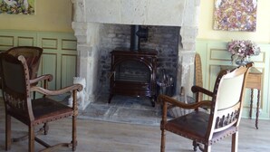 Una habitación rústica con chimenea de piedra, sillas de madera y obras de arte en las paredes.