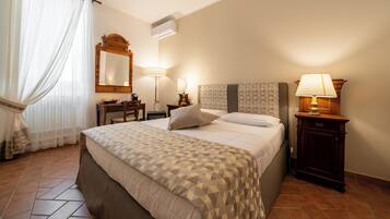 A hotel room with a bed, bedside tables, a mirror, a lamp, and a window with curtains.