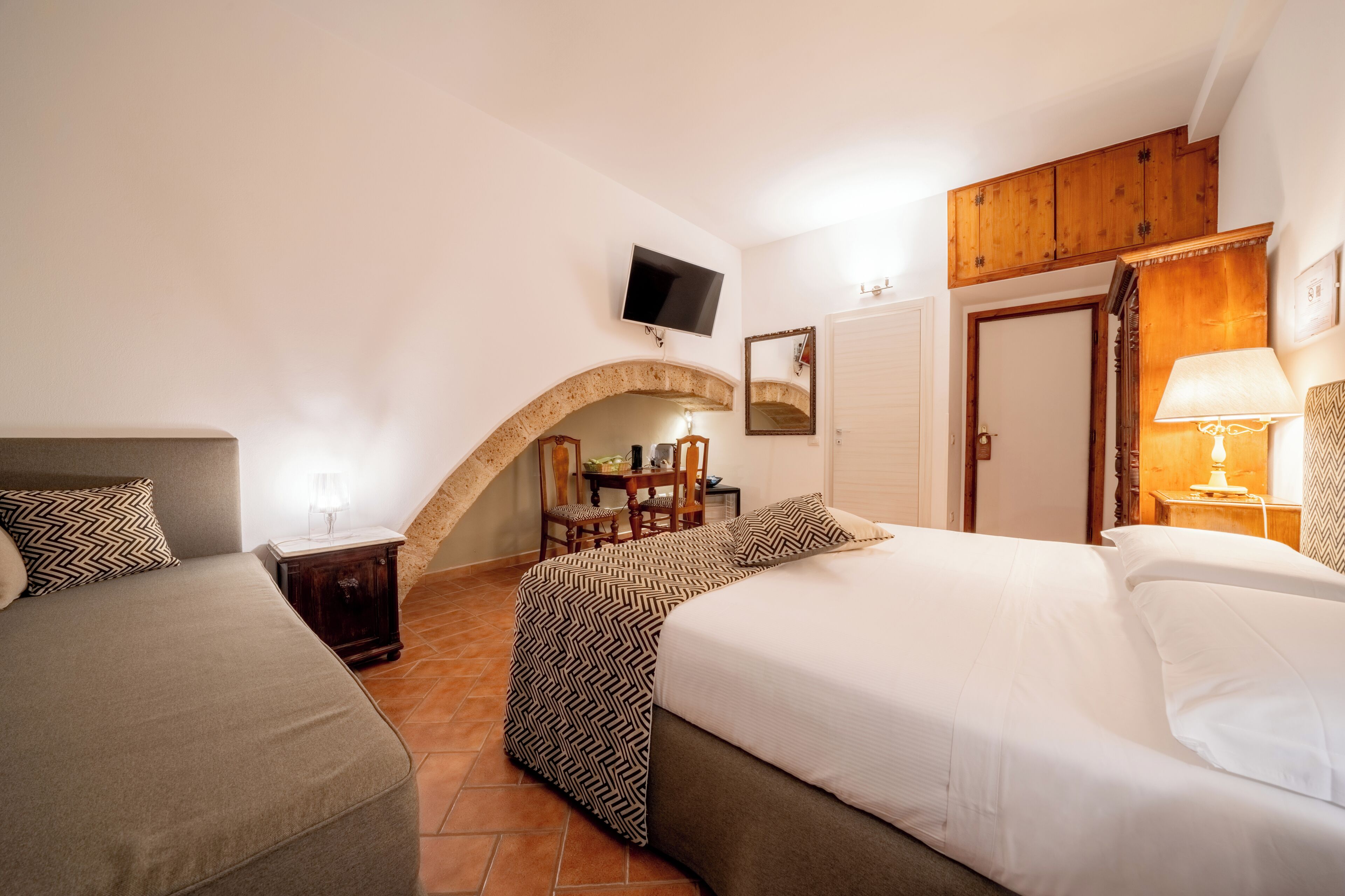 A hotel room with two beds, a TV, a wooden archway, a desk, and a mirror.