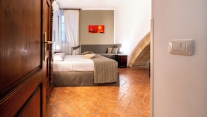 Un dormitorio con una cama, una mesita de noche, un interruptor de luz en la pared y una ventana con cortinas.