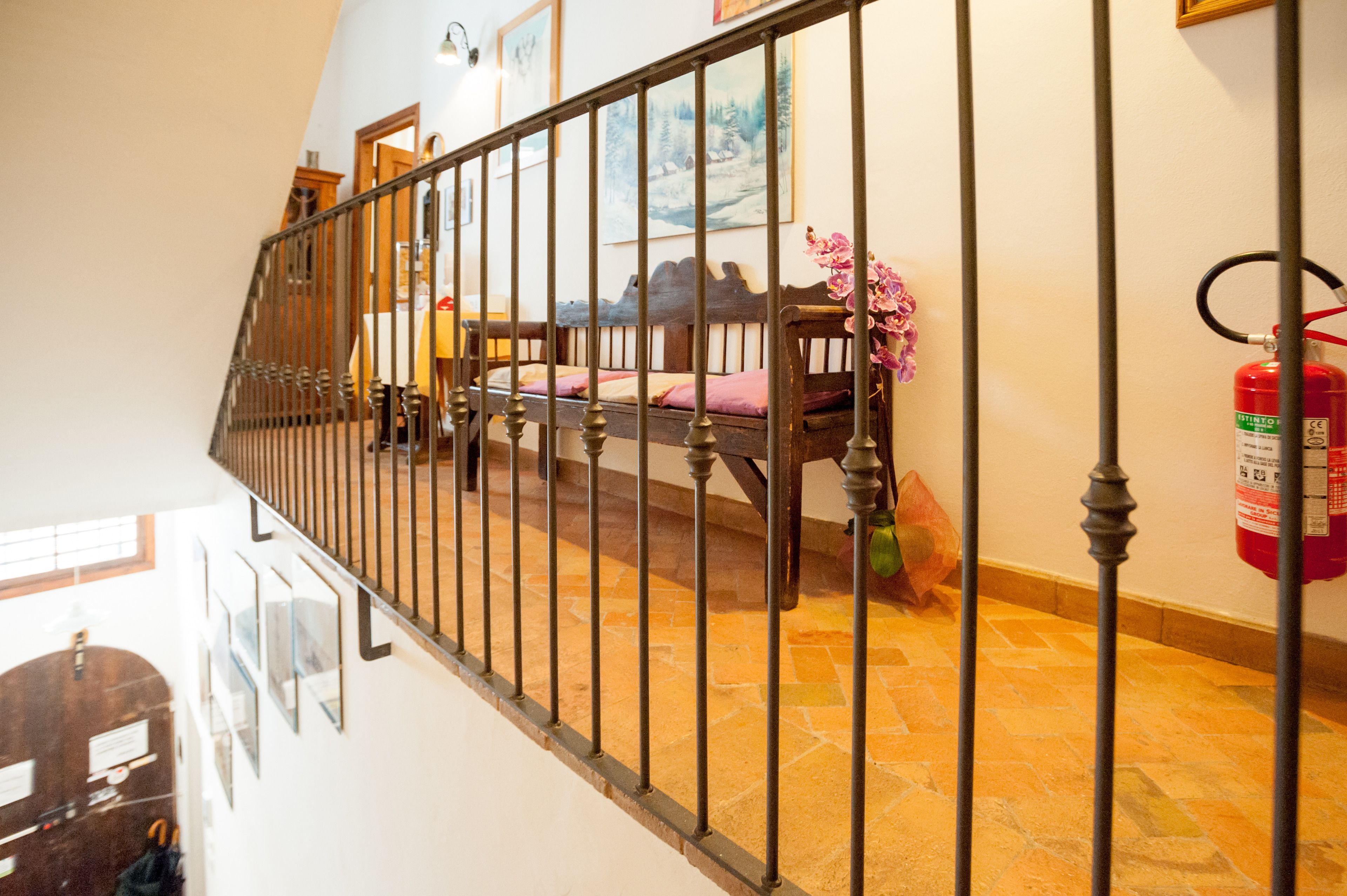 A staircase with a metal railing, a wooden bench, a fire extinguisher, and a painting on the wall.