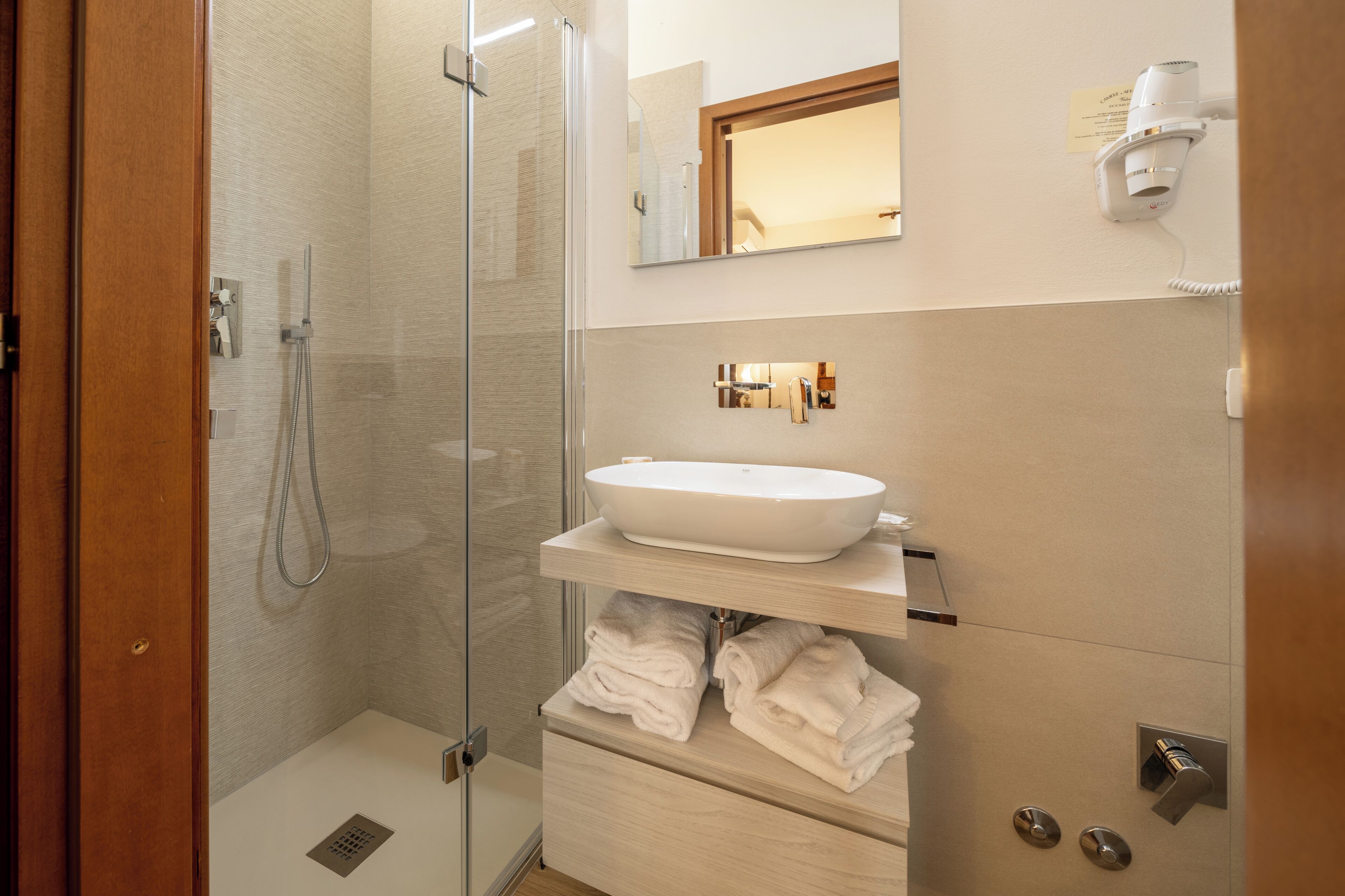 A modern bathroom with a glass shower enclosure, a white sink, and neatly folded towels.