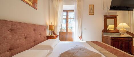 Habitación de hotel con una cama grande, cabecero de madera, televisor, escritorio con lámpara y ventana con cortinas.