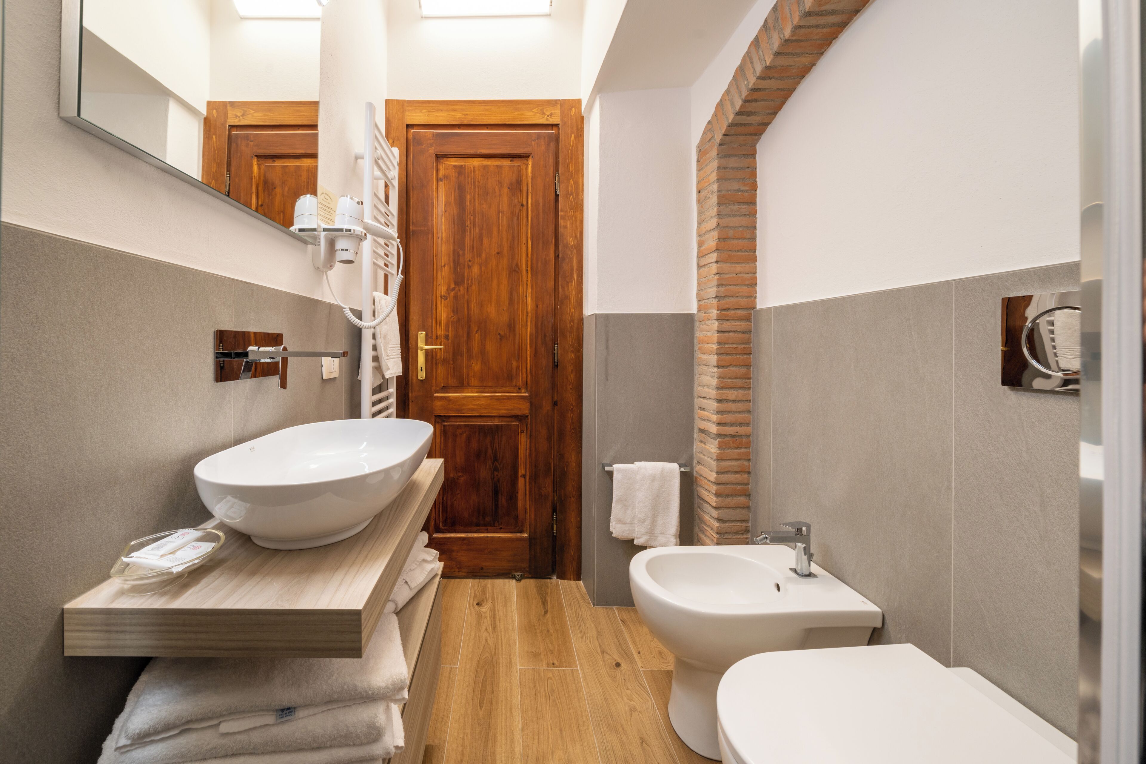 A bathroom with a wooden door, a large sink, a bidet, and a mirror.