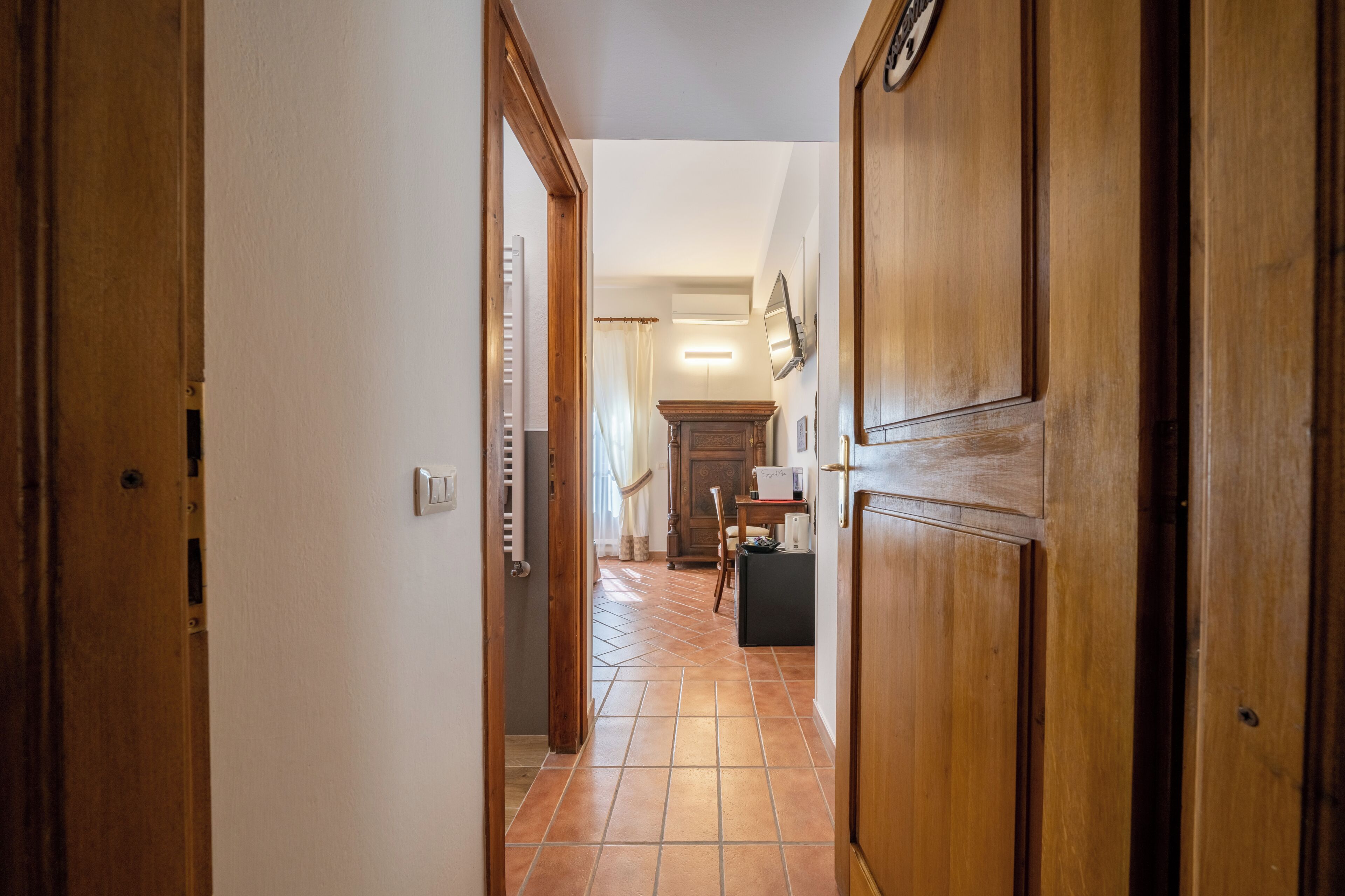 Um corredor com portas de madeira, um radiador, soalho em azulejos e uma mesa com uma cadeira.
