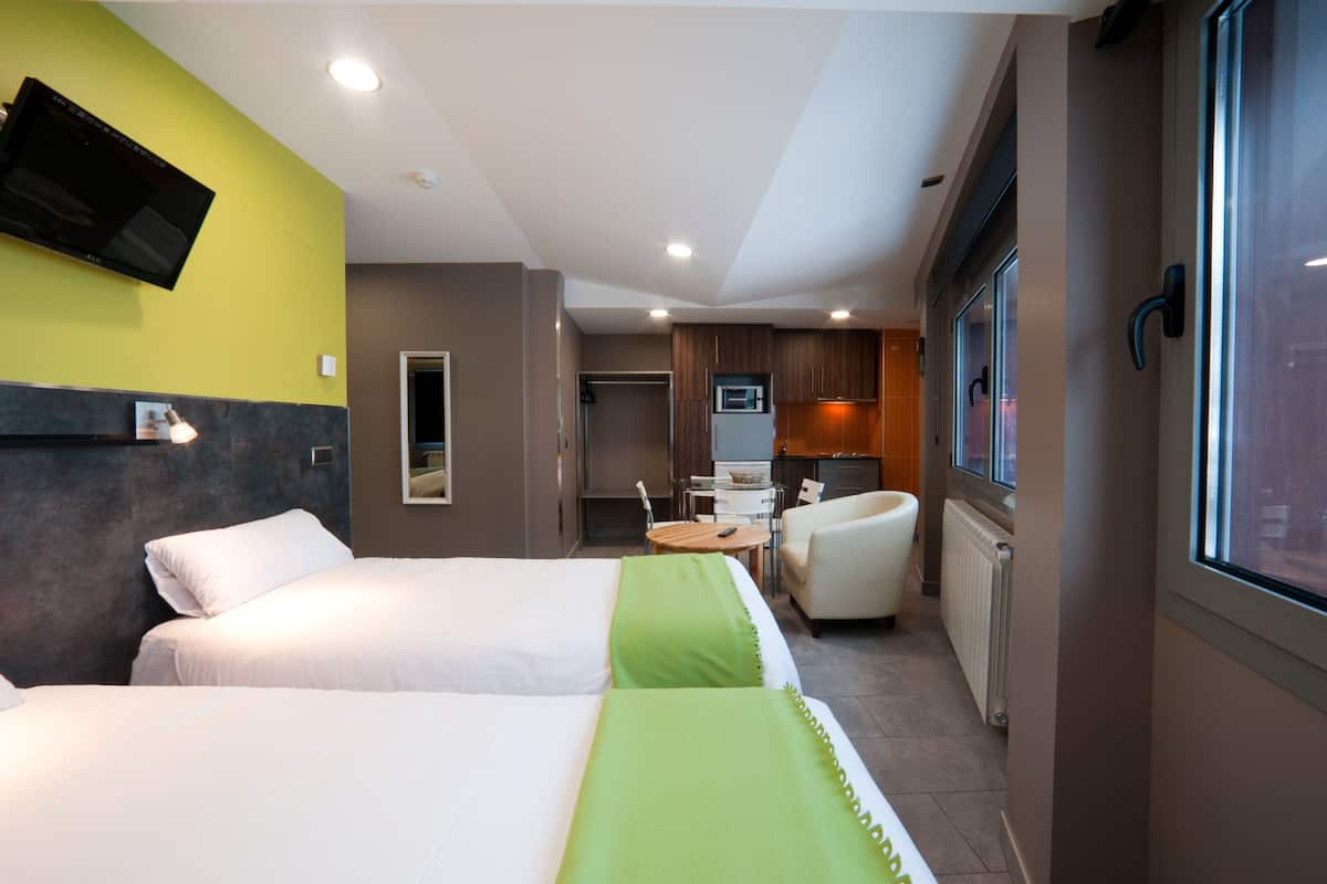 A hotel room with two beds, a television, a small table, a chair, and a window.
