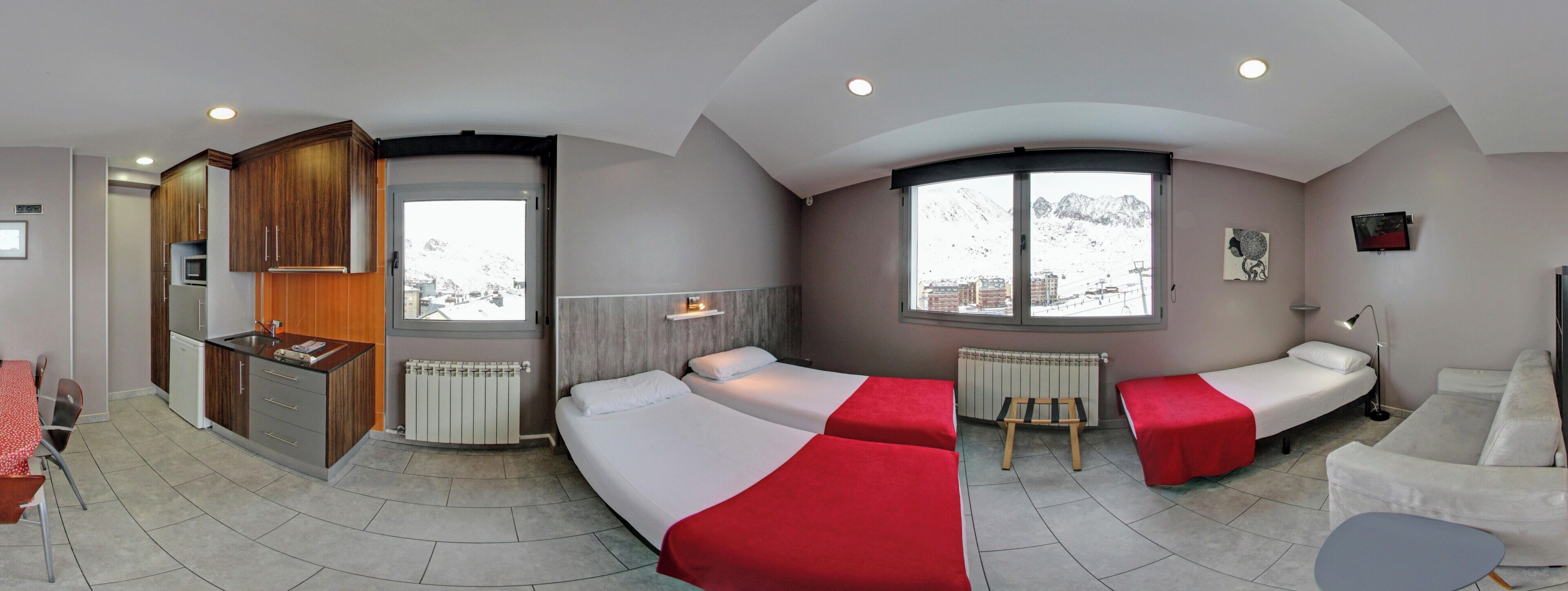 Habitación de hotel con cocina, dos camas, una mesita y televisor.