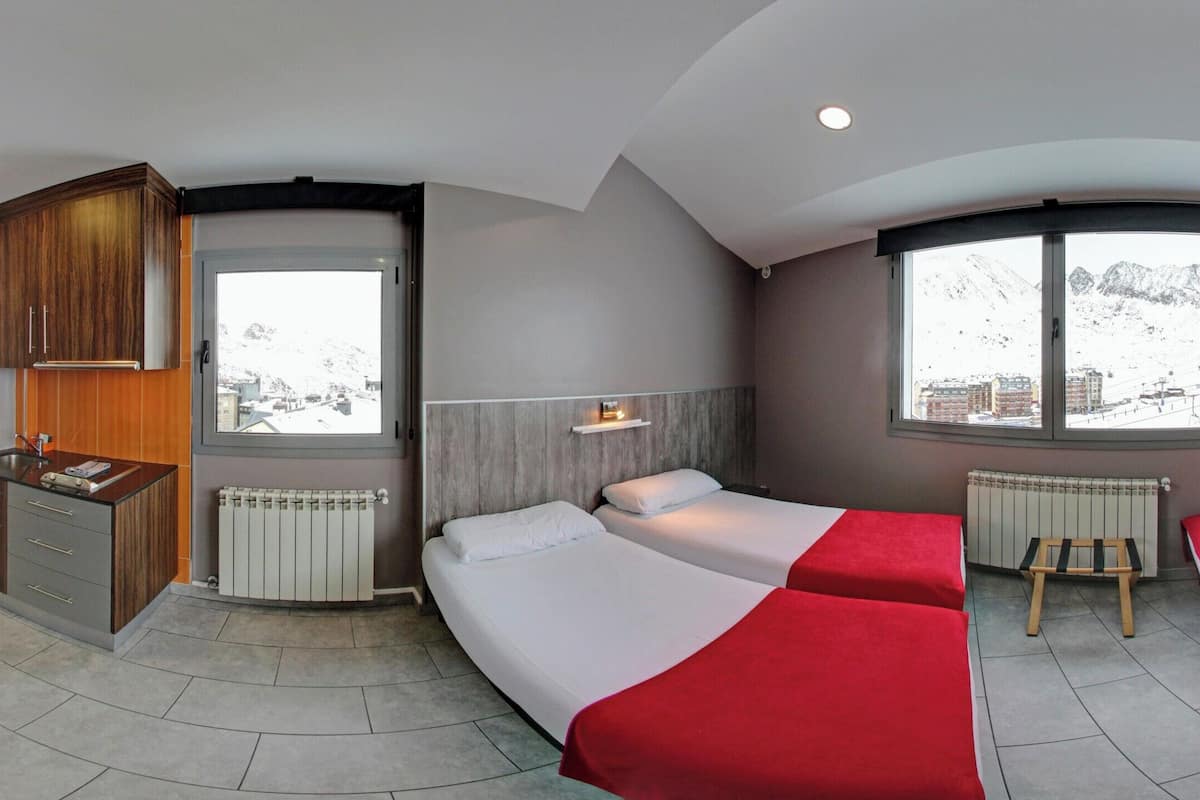 A hotel room with a kitchen, two beds, a small table, and a TV.