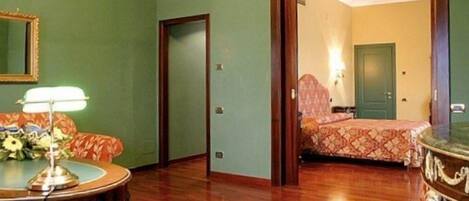 Una habitación de hotel con suelo de madera, cama con edredón estampado, mesita de noche con lámpara y espejo en la pared.