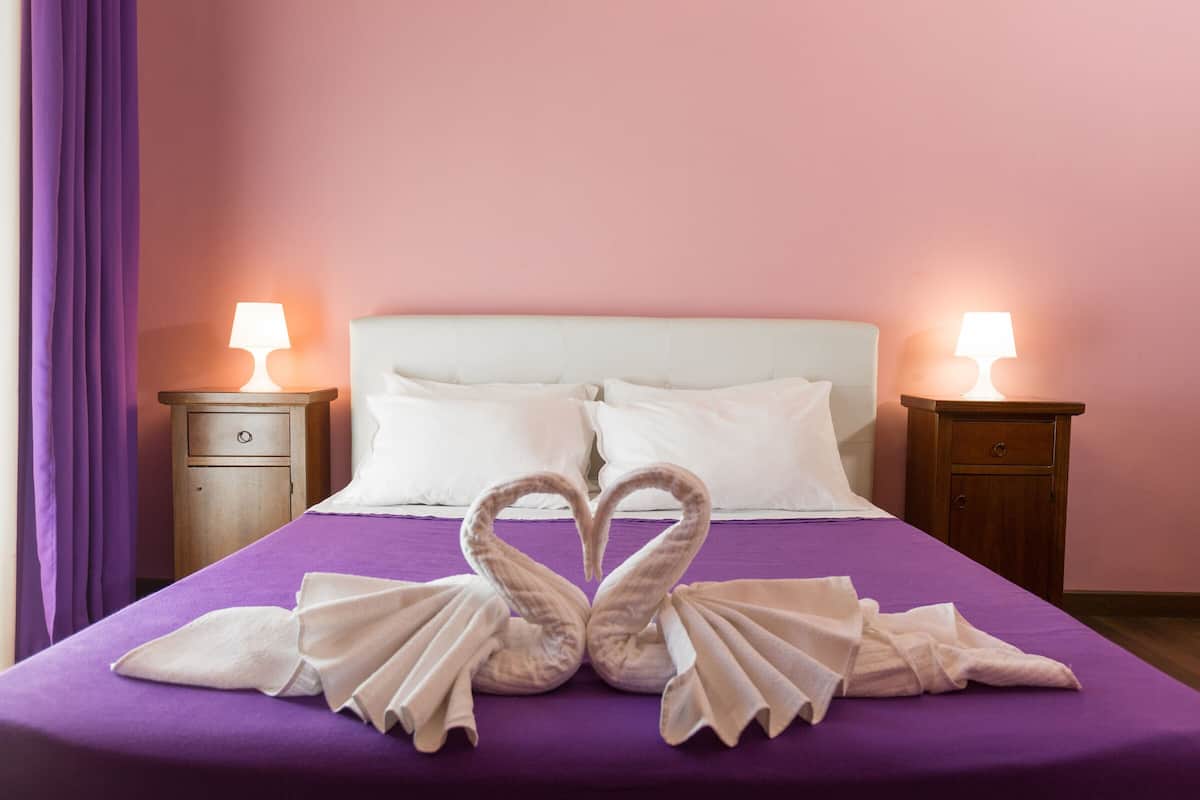 Habitació d'hotel amb un llit, dues taules de nit i un edredó morat.