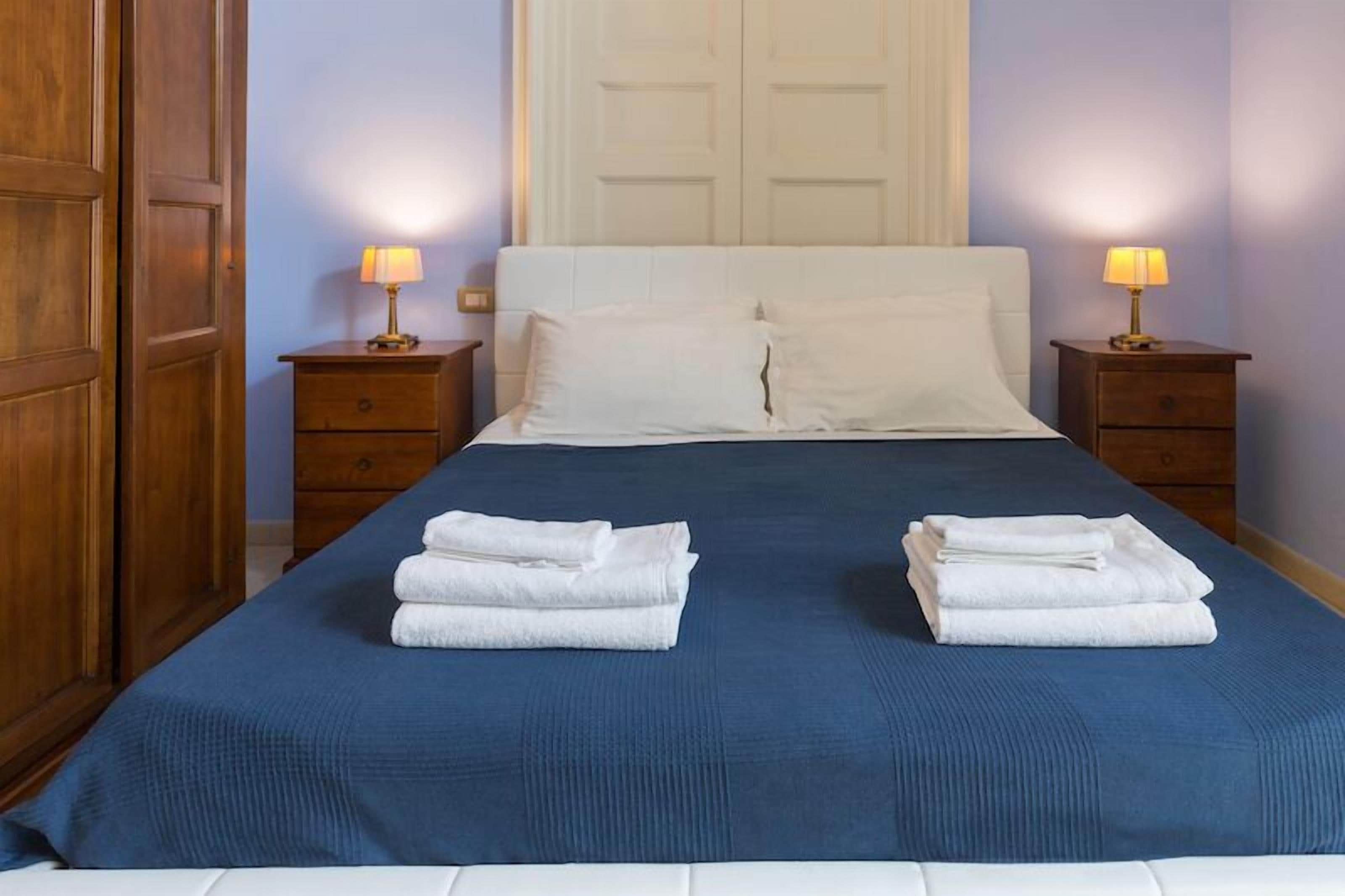 A neatly made bed with a blue bedspread and two white towels folded on the bed.