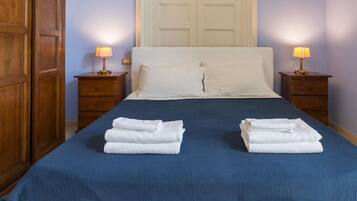 A neatly made bed with a blue bedspread and two white towels folded on the bed.