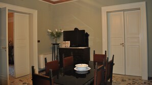 A dining room with a black table, white chairs, a piano, and a vase with flowers. - Teatro Bellini - Bed & Breakfast (Catania)