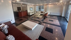 Ampla sala de estar com balcão de recepção, sofá, mesa de centro e tapete estampado.