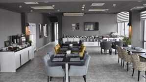 Uma área de refeições moderna com uma mesa comprida, assentos confortáveis e uma cozinha ao fundo.