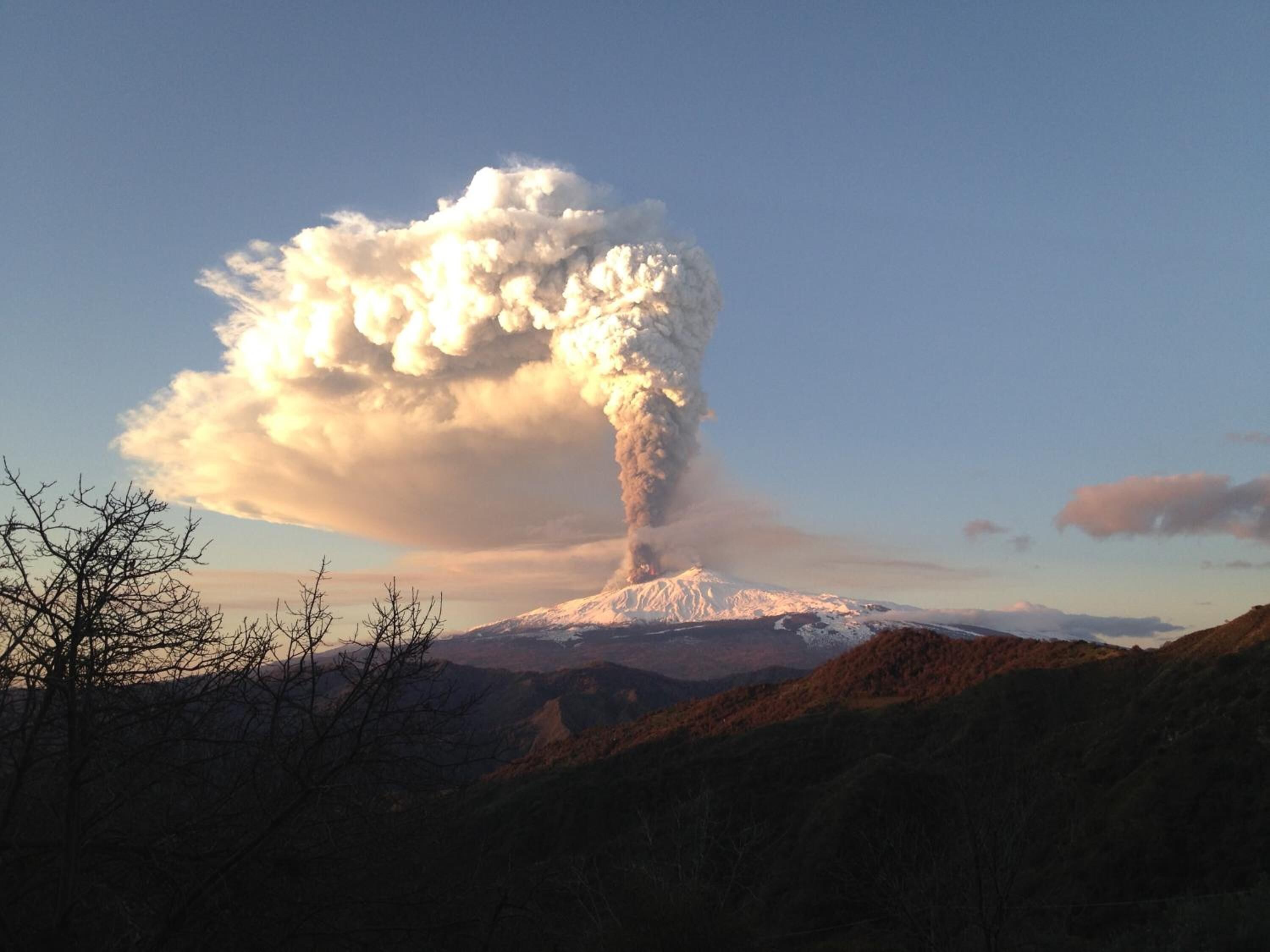 A snow-capped mountain with a large plume of smoke rising from its peak.