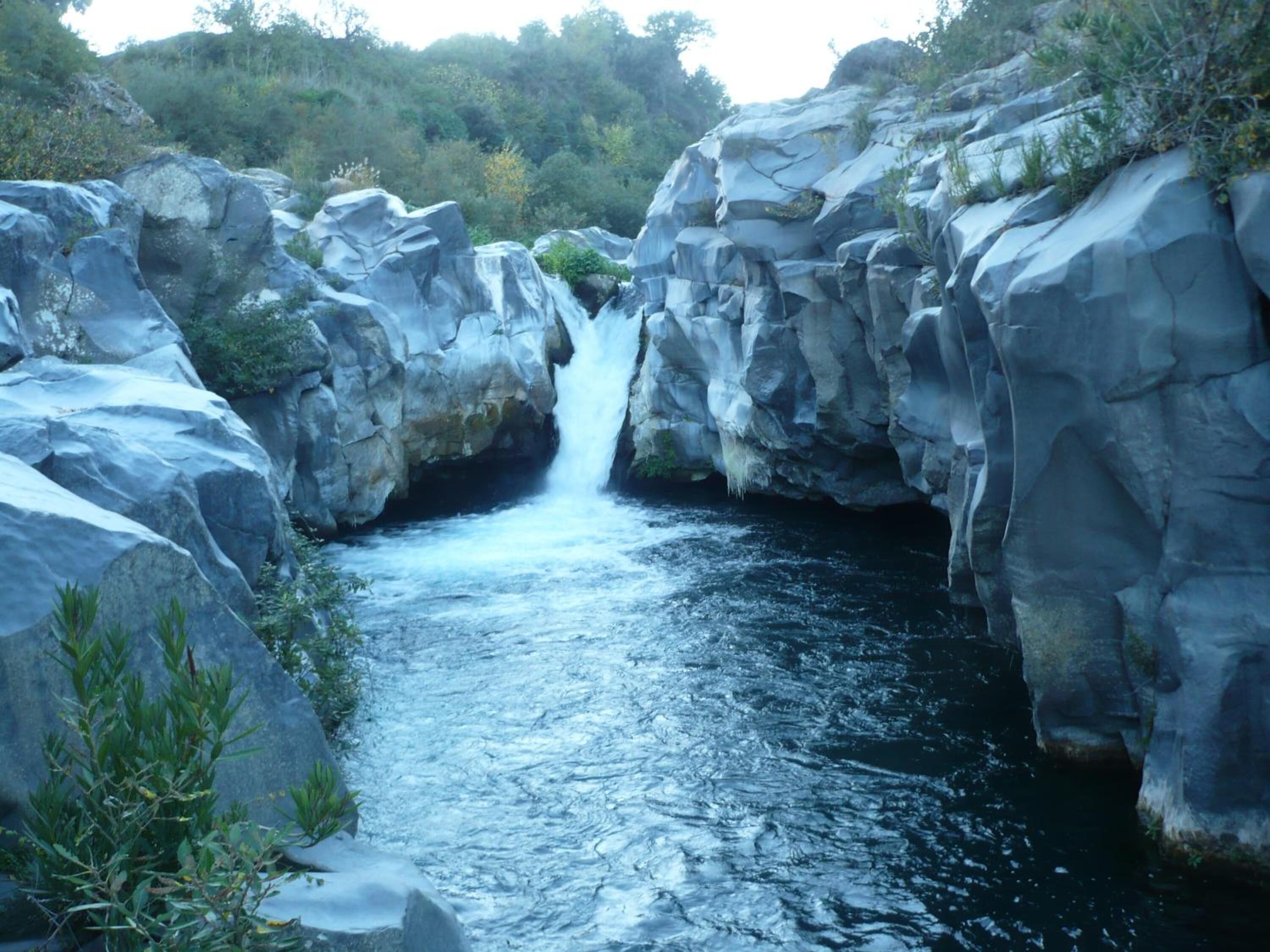 A natural waterfall surrounded by large rocks and greenery.