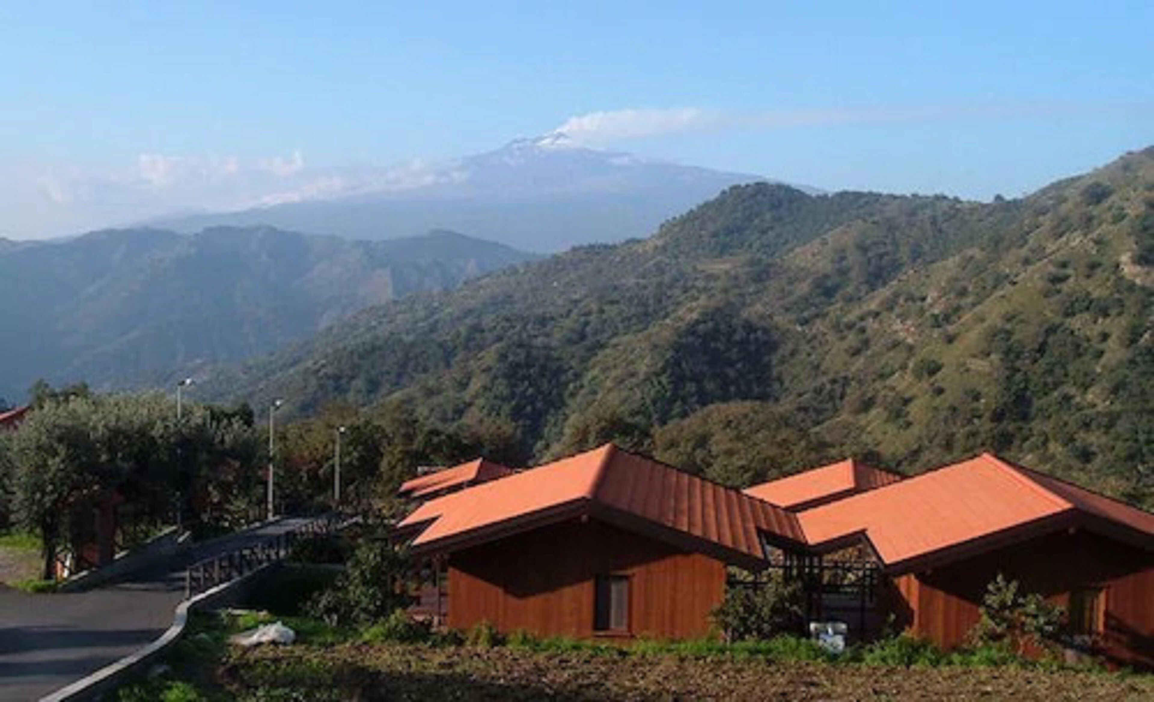 A row of wooden cabins with sloped roofs, set against a backdrop of green hills and a distant mountain range.