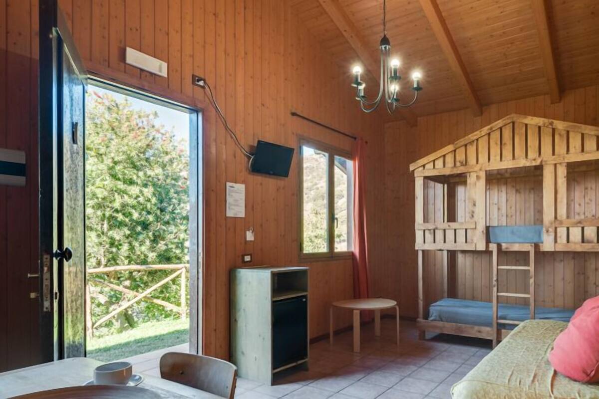 Ein Holzblockhaus-Interieur mit Etagenbett, Essbereich inklusive Tisch und Stühlen sowie einer Pendelleuchte.