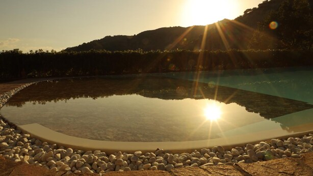 Ein klares Schwimmbecken, umrahmt von einem Kiesstreifen, mit einem Berg im Hintergrund und tief stehender Sonne.