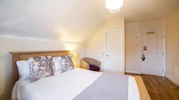 Quarto com uma cama grande, cabeceira de madeira, mesa de cabeceira, uma cadeira e porta com tranca.