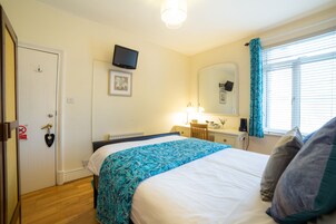 Un dormitorio con cama, escritorio, silla, televisor, espejo y ventana con cortinas.